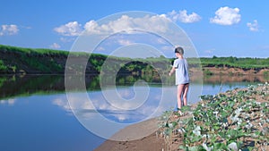 Teen boy is fishing in river using spinning rod at summer sunny day on nature.