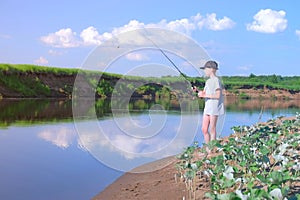 Teen boy is fishing in river using spinning rod at summer sunny day on nature.