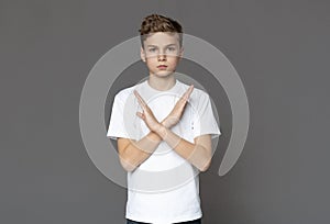 Teen boy gesturing crossed hands, grey studio background