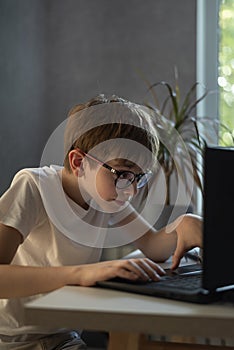 Teen boy in glasses enthusiastically plays computer games. Schoolboy does homework at computer. Homeschooling