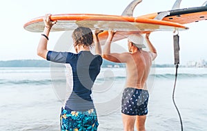 Teen boy with his father with surfboards on the heads walking in the waves on Udawalawe beach in Sri Lanka. Family active vacation