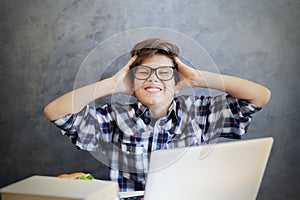 Teen boy holding his head and using laptop