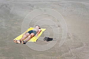 Teen boy lies on yellow towel and sunbathes on the beach. Traveling on an airplane with children.