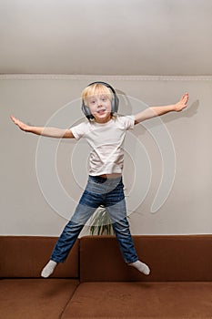 Teen boy listening to music on headphones and jumping on couch. Vertical frame