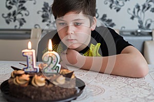 Teen boy looks thoughtfully at cake with candles on twelfth day of birth