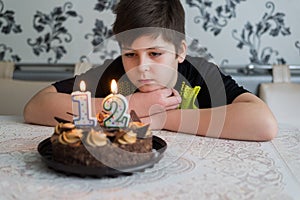 Teen boy looks thoughtfully at cake with candles on twelfth day of birth