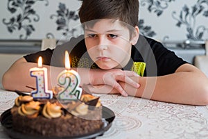 Teen boy looks thoughtfully at cake with candles on twelfth day of birth
