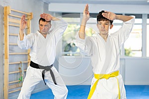 Teen boy and middle-aged man wearing kimono training karate techniques