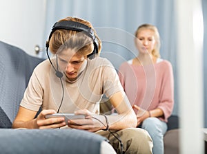 Teen boy playing game on phone against background of frustrated mother