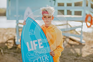 Teen boy posing and making faces with surfboard against lifeguard tower.