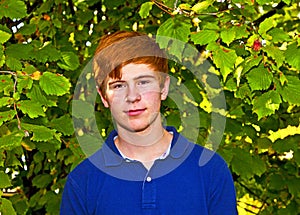 Teen boy with red hair standing in front of a hedge