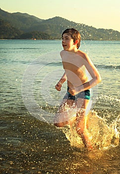 Teen boy runnung in the sea on mountain beach background smiling