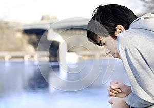 Teen boy sadly looking out over river, thinking photo