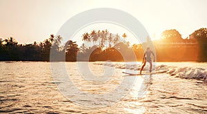 Teen boy silhouette riding a long surfboard. He caught a wave in an Indian ocean bay with magic sunset background. Extreme water