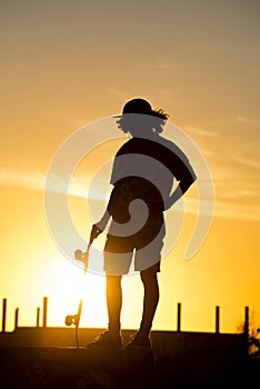 Teen boy silhouette with skateboard at sunset