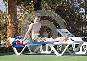 Teen boy sits on a sun lounger