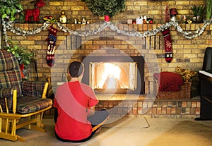 Teen boy sitting in front of roaring fire in brick fireplace dec