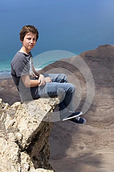 Teen boy sitting on a rock at the coast