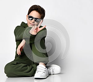 Teen boy in sportswear and sunglasses sitting on a gray background.