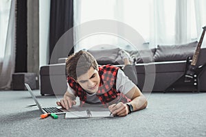 teen boy studying with copybook and laptop while lying