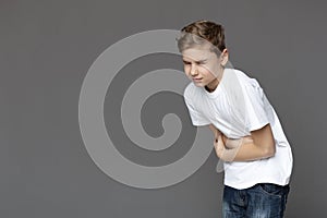 Teen boy suffering from stomachache, grey background photo