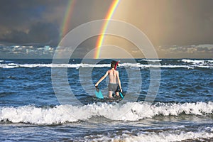 Teen boy in the swim flippers snorkeling mask and tude in the sea wave on the rainbow background