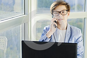 Teen boy talking over mobile phone and using laptop