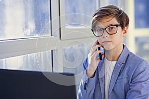 Teen boy talking over mobile phone and using laptop