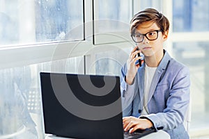 Teen boy talking over mobile phone and using laptop