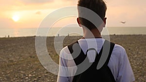 Teen boy walking on the beach in the evening at sunset