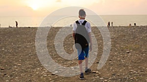 Teen boy walking on the beach in the evening at sunset