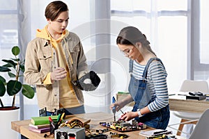 teen boy watching how female teenager brazing computer circuit with soldering iron