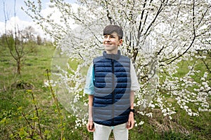 Teen boy wear sleeveless vest against white blloming tree in spring