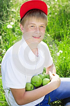 Teen boy is wearing red cap holding apples