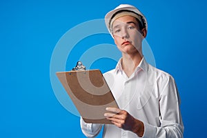 Teen boy in white hardhat writing on clipboard against blue background