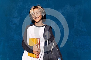 Teen boy in wireless headphones with books and backpack