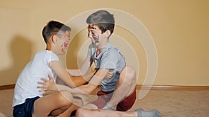 Teen boys with hands and faces in colorful paints sitting on floor play with each other