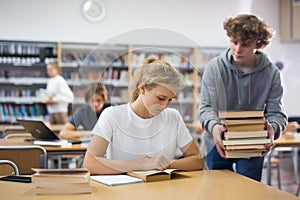 Teen brings stack of book to his girlfriend in school library