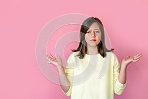 Teen brunette girl frowns on a pink background