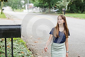 A teen brunette girl with long hair checking the mailbox for letters and packages.