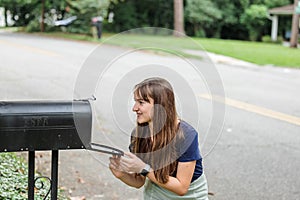 A teen brunette girl with long hair checking the mailbox for letters and packages.