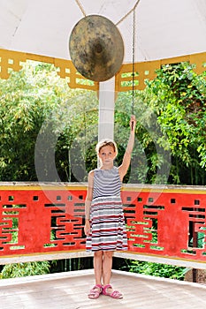 Teen caucasian girl beating gong in classical chinese pavilion