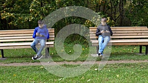 Teen cell phone, video game, social media addiction. Teenage boys sitting on wooden park bench apart and using mobile