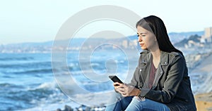 Teen checking phone and looking at horizon on the beach