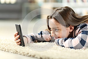 Teen checking smart phone lying on a carpet at home