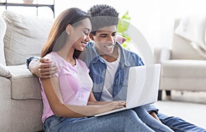 Teen couple with laptop sitting on floor and browsing internet