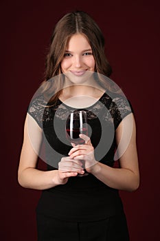 Teen in dress holding glass of wine. Close up. Dark red background