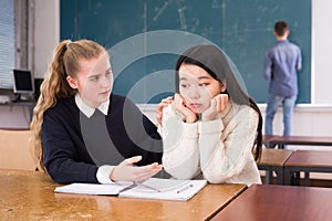 Teen female student supporting upset Chinese girl in classroom