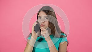 Teen female talking using cell phone in studio against pink background. Slow motion