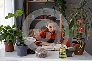 Teen gardener taking care and transplanting houseplants into a new ceramic pot and reading old book on the wooden table